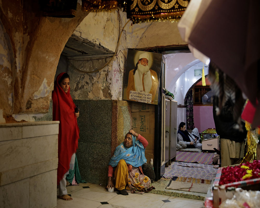 An Indian Muslim devotee, left, walks as a woman asks for alms outside the Nizamuddin Dargah, the burial site of revered Sufi saint Nizamuddin Auliya, in New Delhi - AP