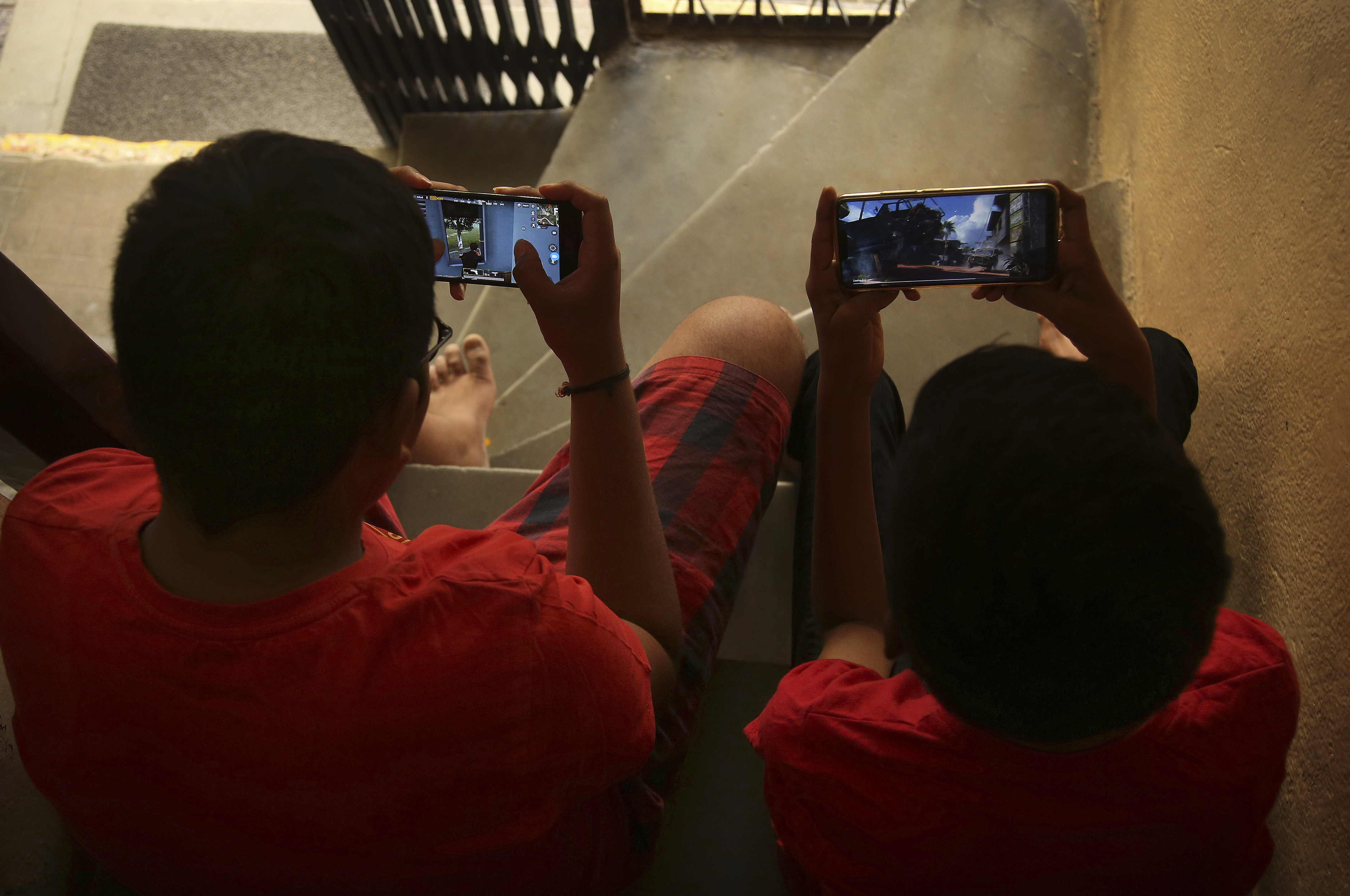 Indian children play online game PUBG on their mobile phones sitting on stairs outside their house in Hyderabad - AP