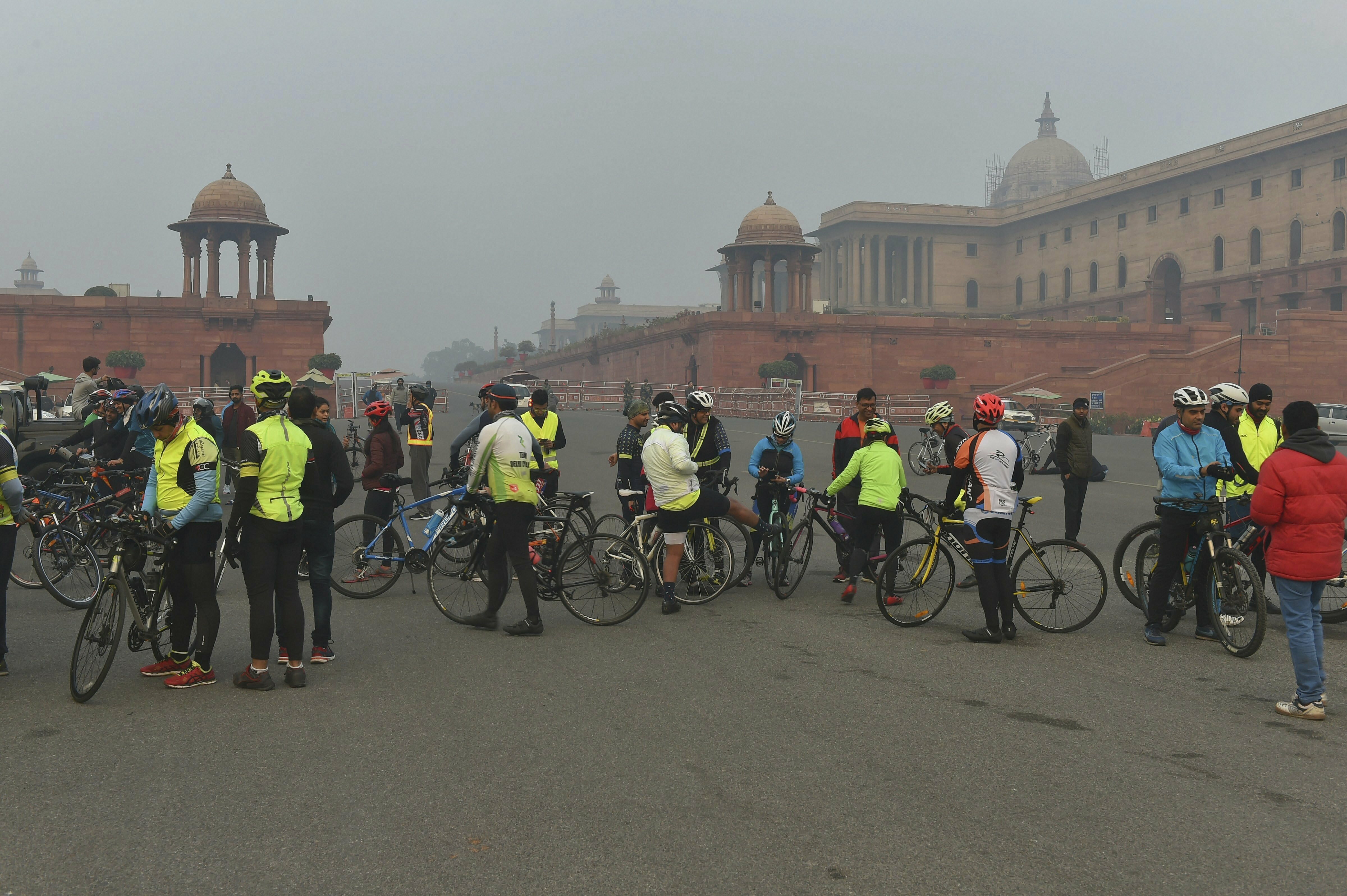 Cyclists rest near South and North block buildings, enveloped in fog on a cold, foggy morning, in New Delhi - PTI