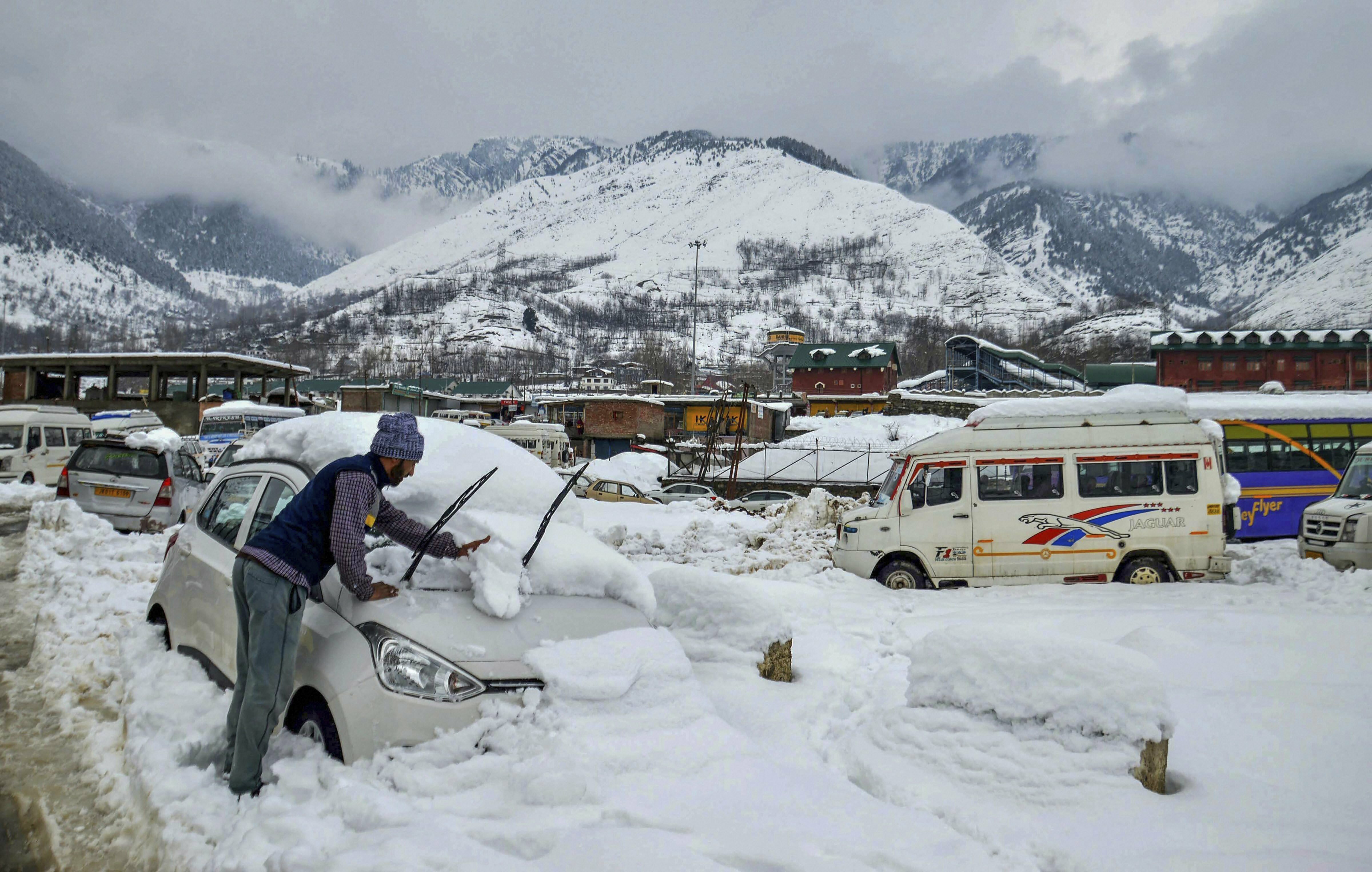 A man clears snow off a car near Banihal railway station, in Ramban district - PTI