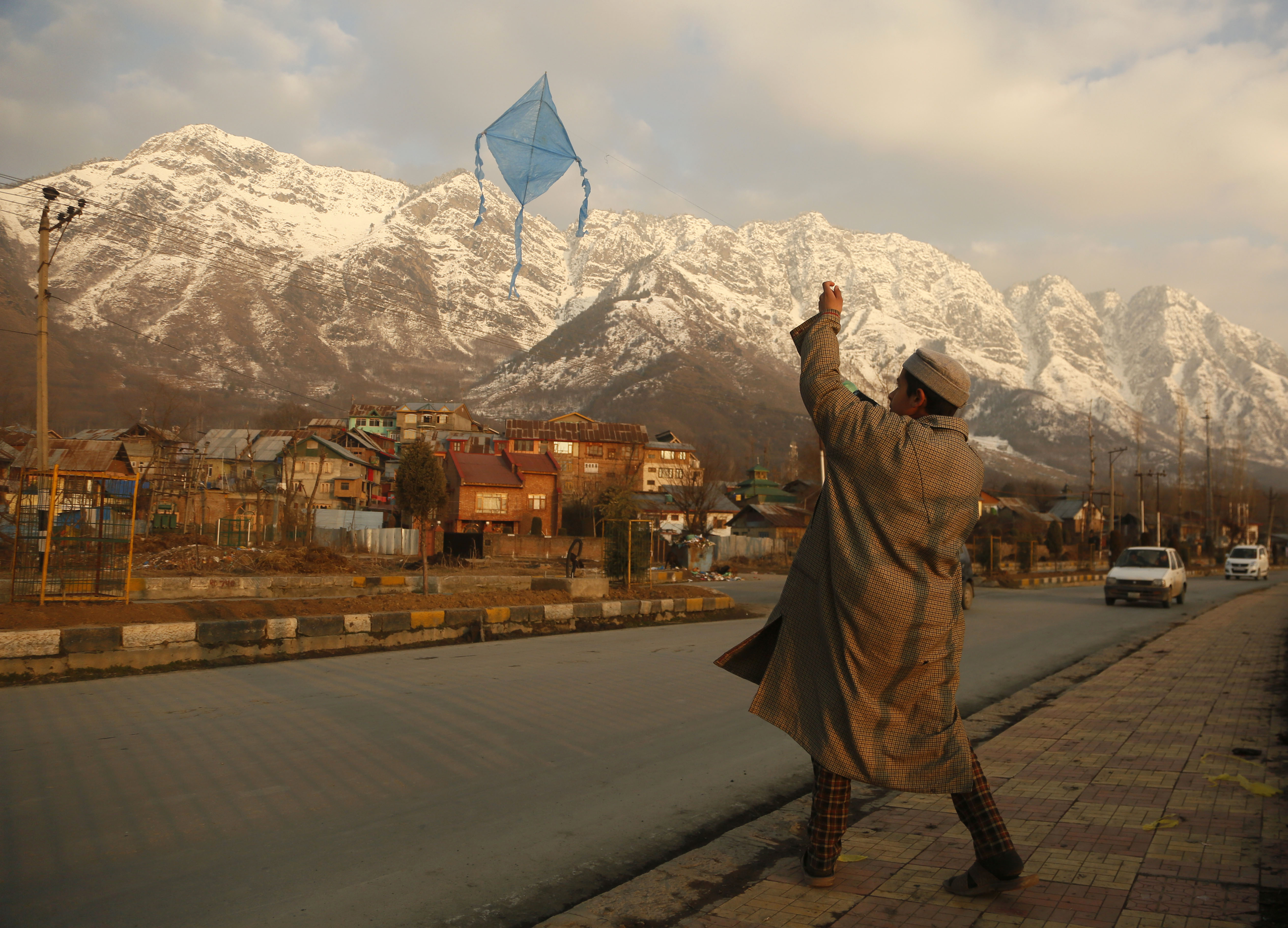 A Kashmiri boy flies a kite in the backdrop of snow clad mountains on a sunny day in Srinagar - AP