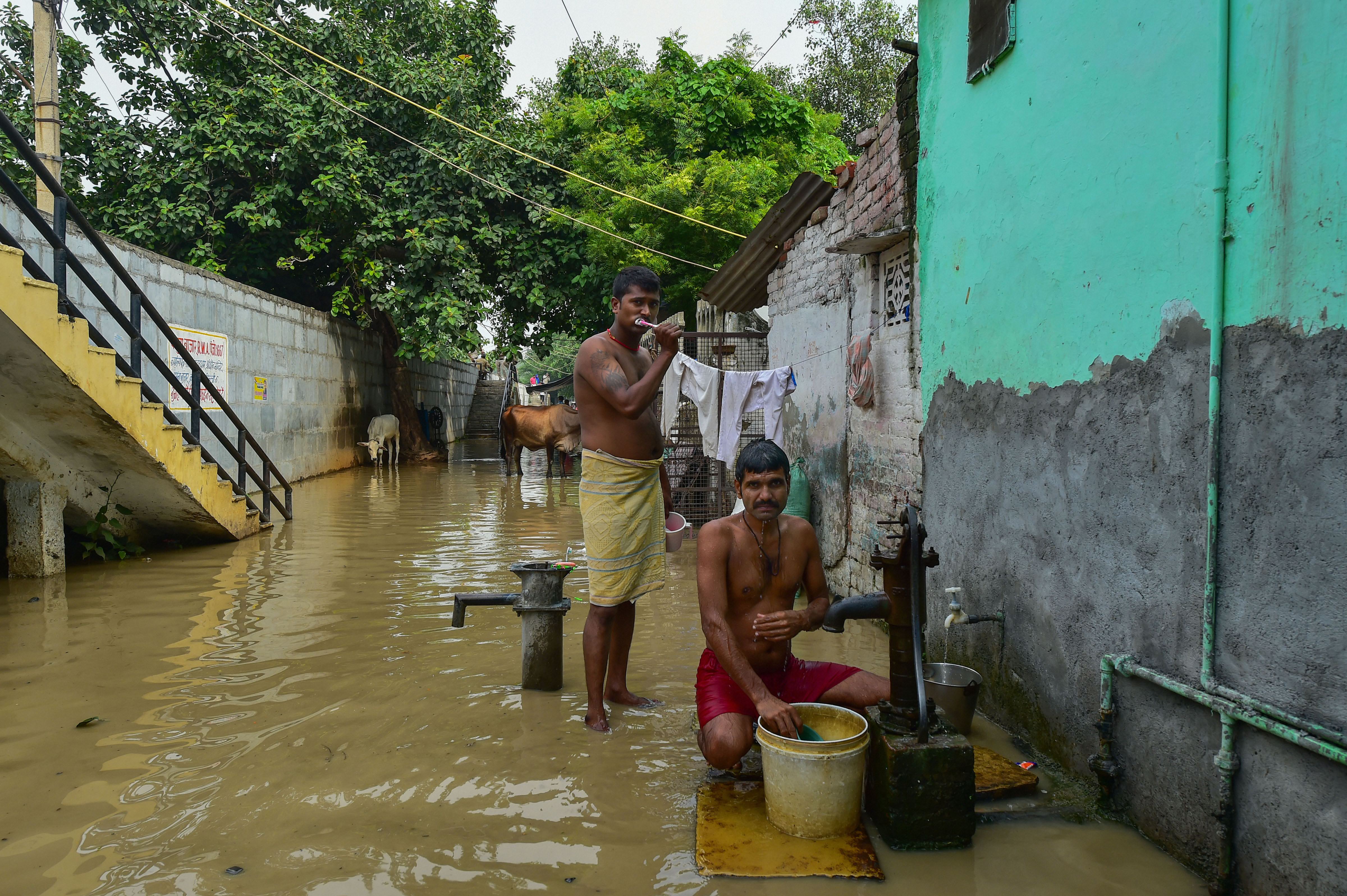 Residents busy doing everyday chores in a flooded locality along the banks of  Yamuna river after rise in its water level following release of water from the Hathinikund Barrage - PTI