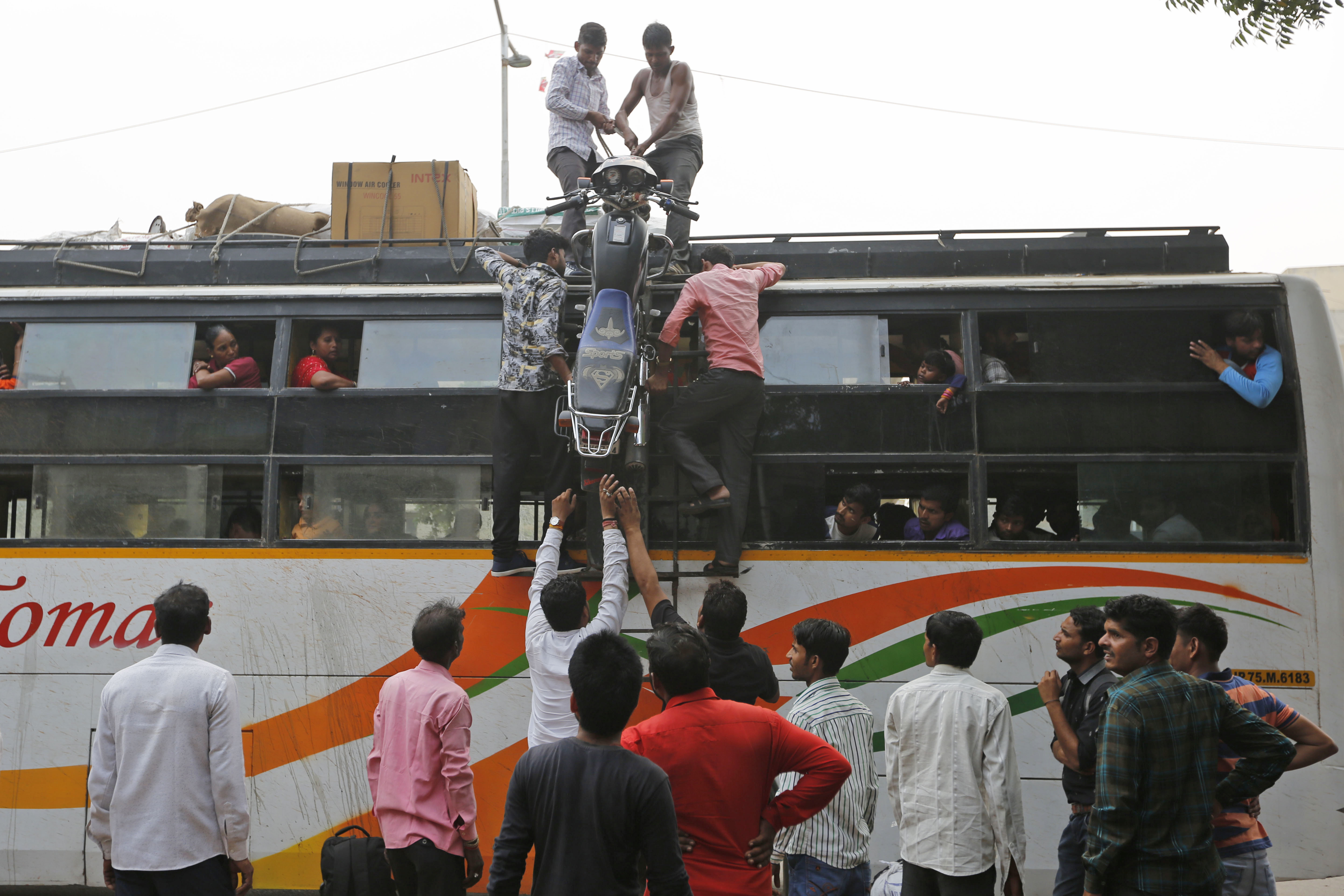 Indians load a motorcycle onto a bus headed to Uttar Pradesh, in Ahmadabad, India - AP